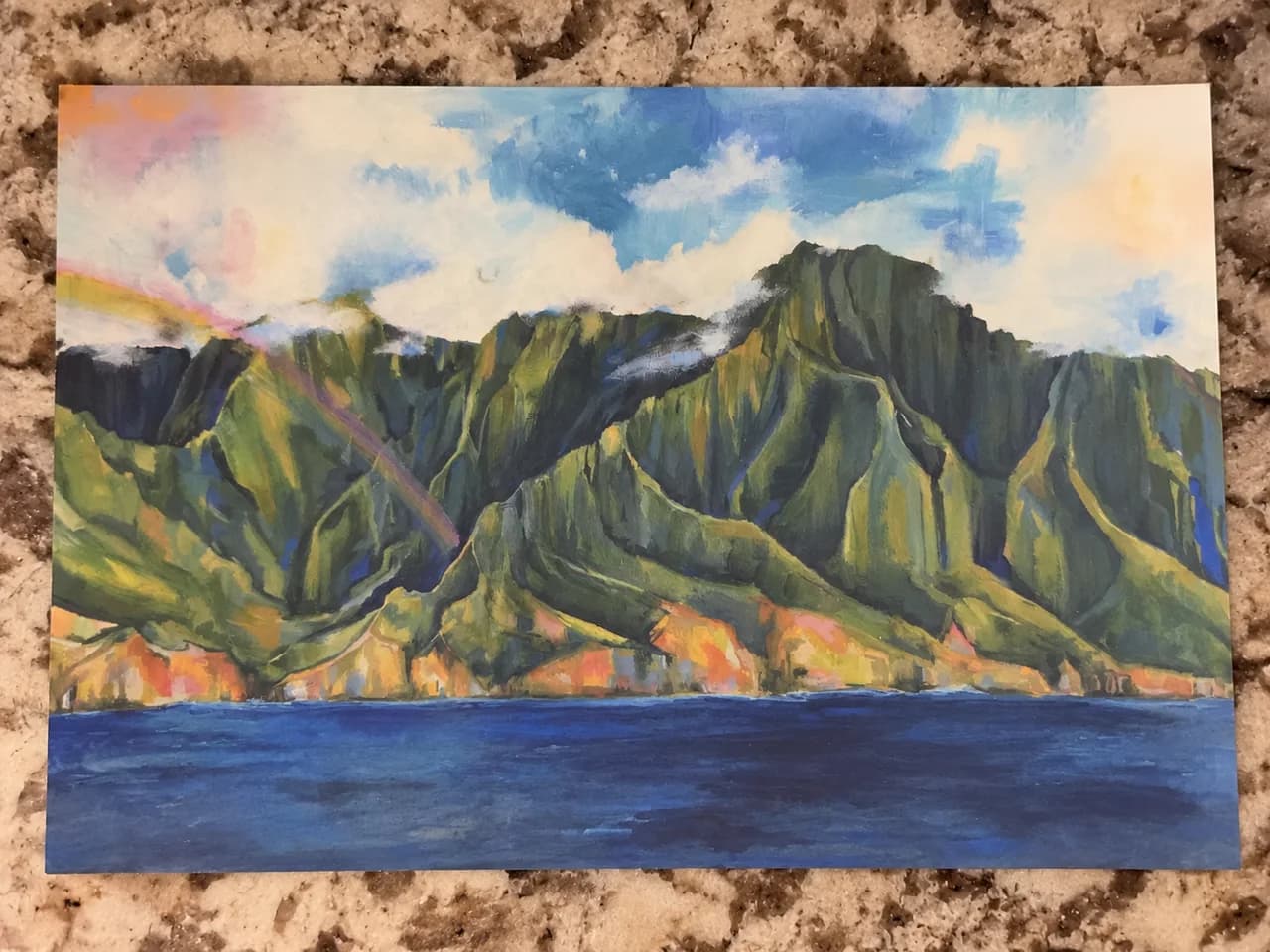 A colorful mountain and ocean postcard resting on a stone countertop